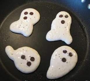 Spooky Halloween ghost pancakes topped with whipped cream and chocolate eyes.