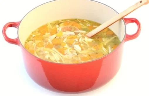 A bowl of homemade chicken noodle soup with vegetables and noodles in a pot.